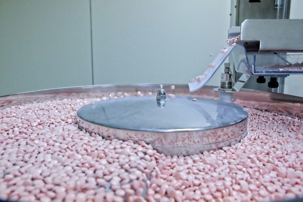 Small pink pills tumbling on a machine surface